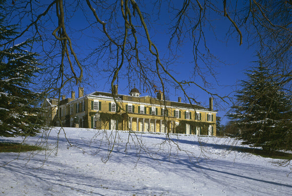 Polesden Lacey house viewed through twiggy trees in winter with snow lying